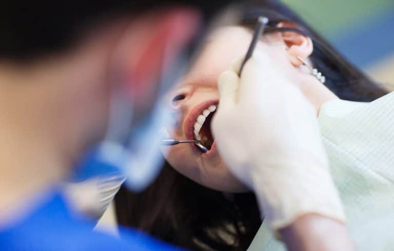 Dentist applying dental veneers at Midland Dental Hub to enhance a patient's smile by covering crooked, gapped, chipped, misshapen, or discoloured teeth, resulting in a more even and attractive appearance